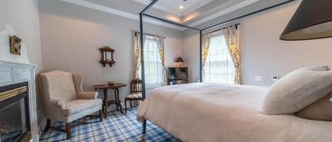 A bedroom with a bed, a chair, a small table, a fireplace, and a ceiling fan.