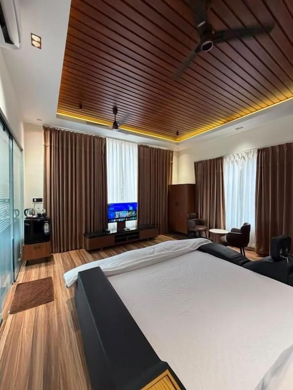 Une chambre d’hôtel avec un grand lit, une télévision, un bureau avec une chaise et une fenêtre avec des rideaux.