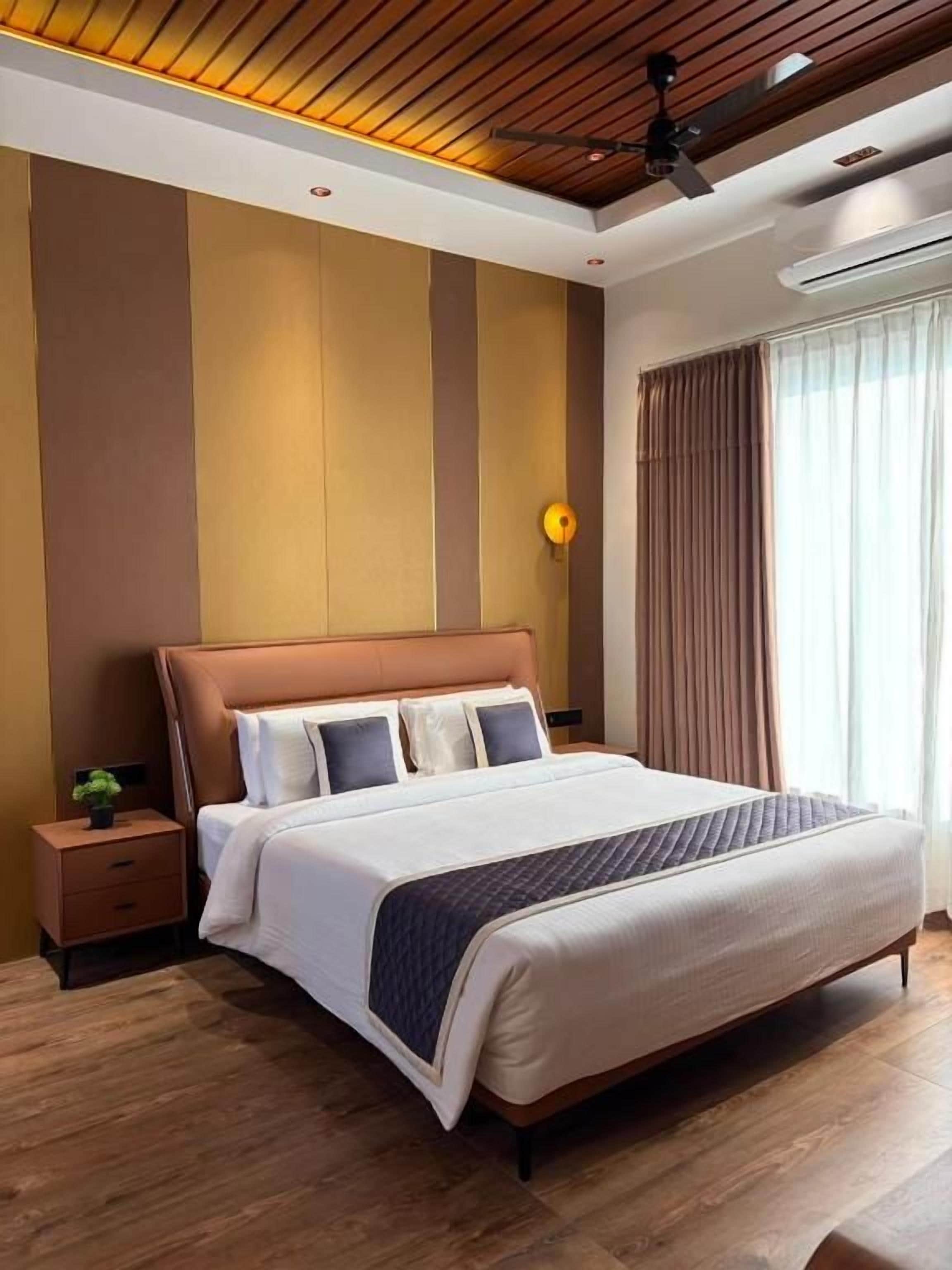 Una moderna camera d'albergo con un letto grande, un comodino, una lampada da notte, una ventola a soffitto e una finestra con tende.