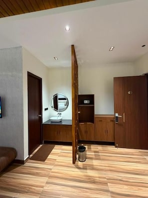 Une pièce avec un plancher en bois, une armoire en bois, un miroir, un lavabo et une porte.