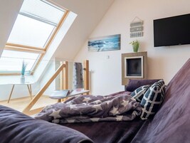 A bedroom with a sloped ceiling, a bed with a star-patterned blanket, a television, and a painting of the ocean.