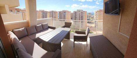 A balcony with a sofa set, a table, and chairs, overlooking a cityscape.