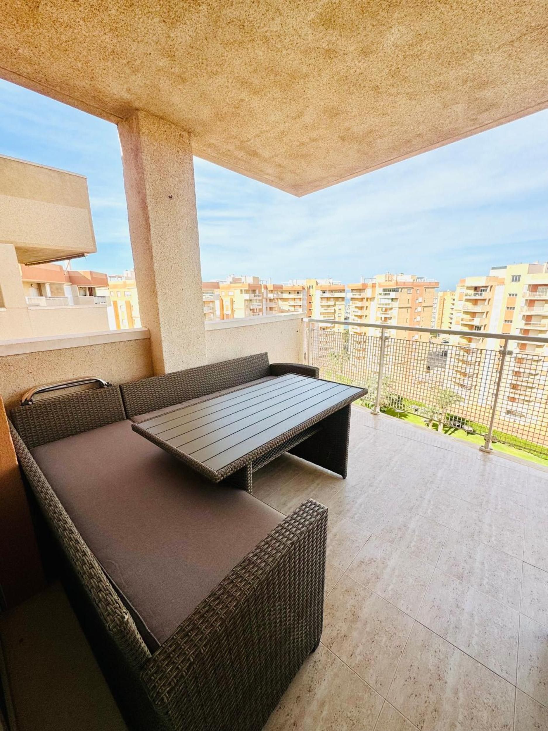 En balkon med en fletsofa og et bord, med udsigt over et boligområde.