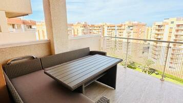 En balkon med en fletsofa og et bord, med udsigt over et boligområde.