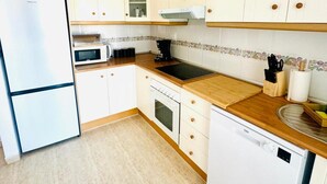 Eine Küche mit weißen Schränken, einem Kühlschrank, einer Mikrowelle, einem Backofen und einem Geschirrspüler.