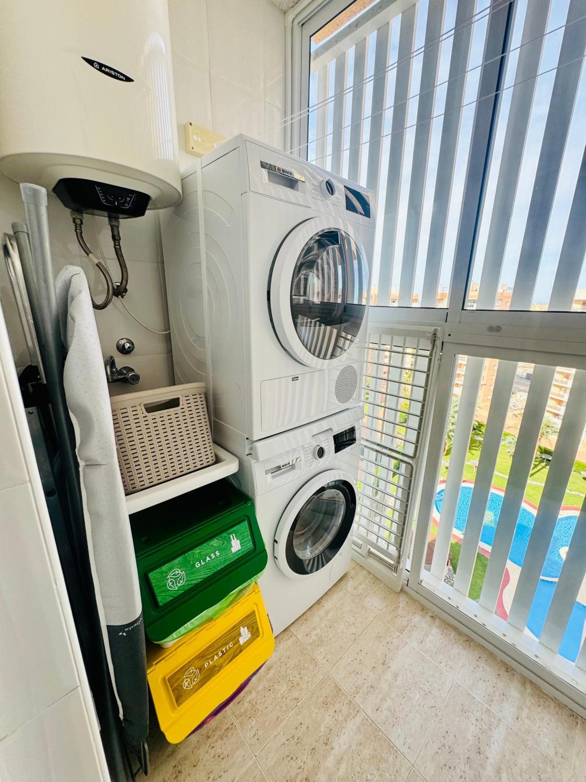 A compact laundry area with a Bosch washing machine, a drying rack, and plastic storage bins.