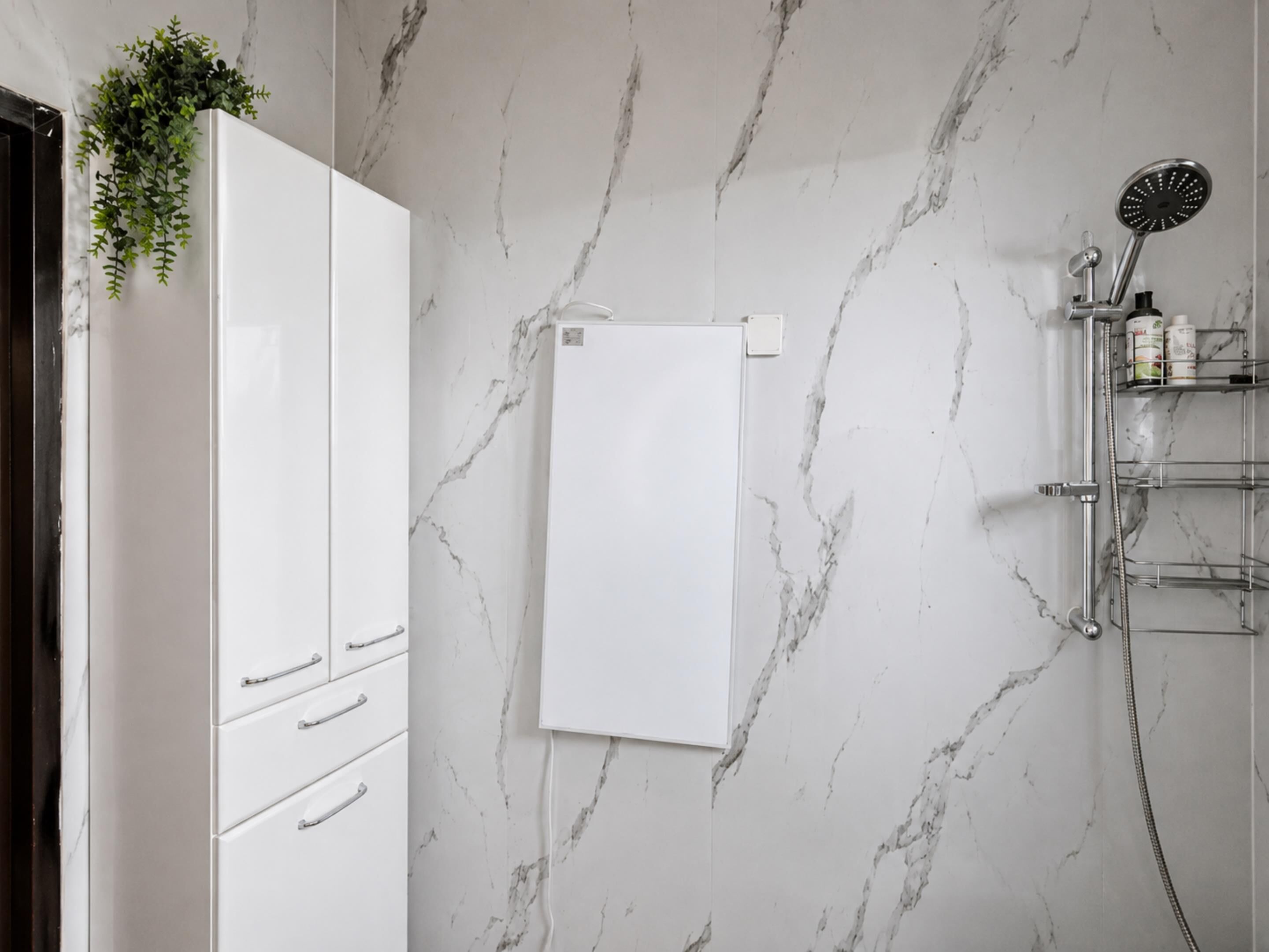 Ein Badezimmer mit Marmorwand, einem weißen Schrank mit Schubladen, einer Dusche mit Handbrause und einem Ablagefach für Toilettenartikel.