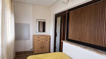 Ein Schlafzimmer mit einem Bett, einem Holzschrank, einem Spiegel und einem Fenster mit Jalousien.