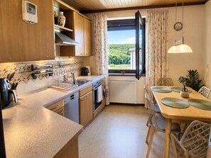 Una cocina con armarios de madera, horno empotrado, cafetera y una ventana con cortinas.