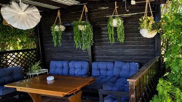 Ein überdachter Außenbereich mit einem Holztisch und blauen, gepolsterten Sofas.