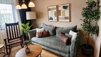 Ein Wohnzimmer mit grauem Sofa, einem Holztisch und einer Topfpflanze.