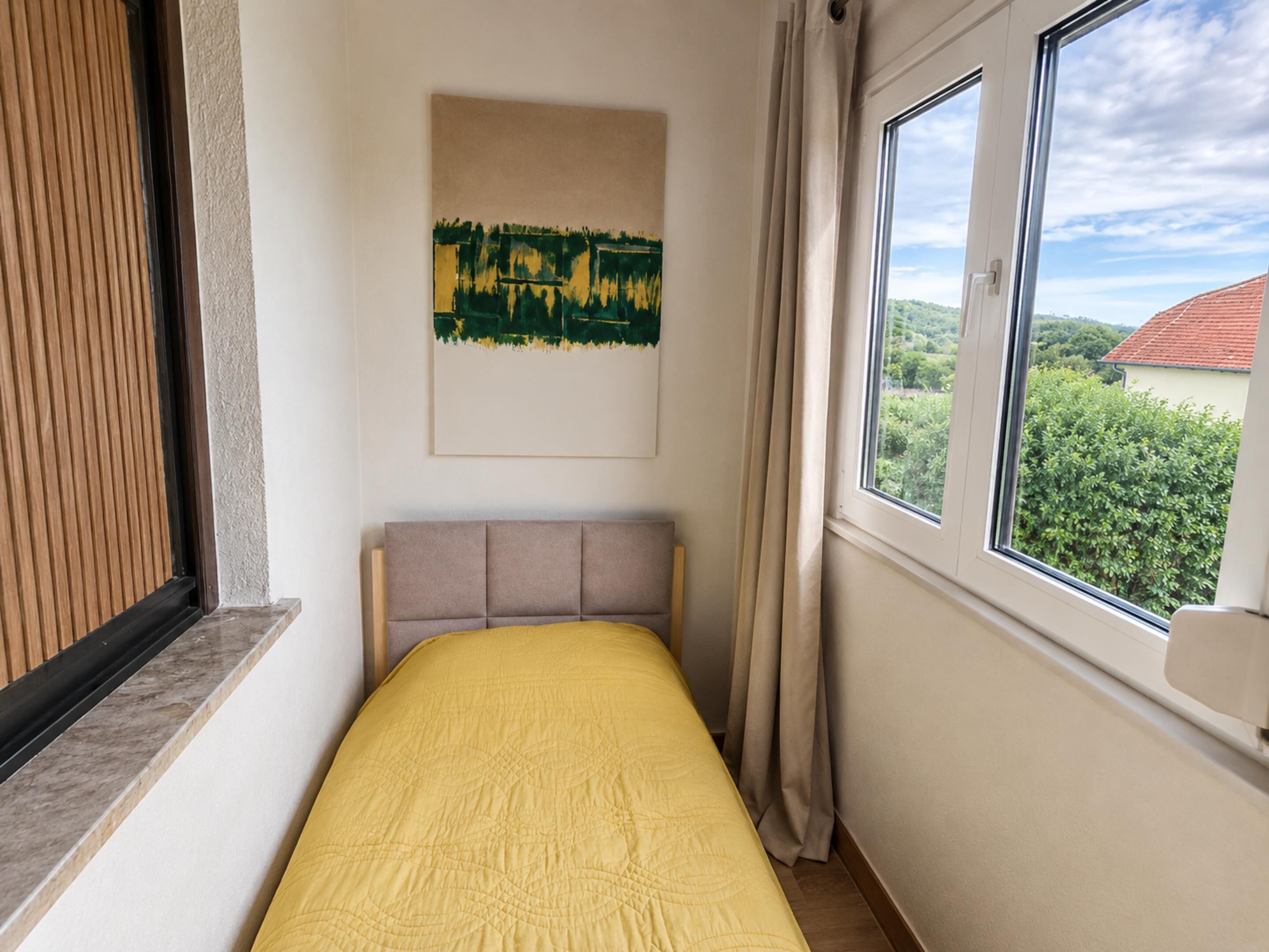 Una habitación con una cama, una ventana con vistas a zonas verdes y un cuadro en la pared.