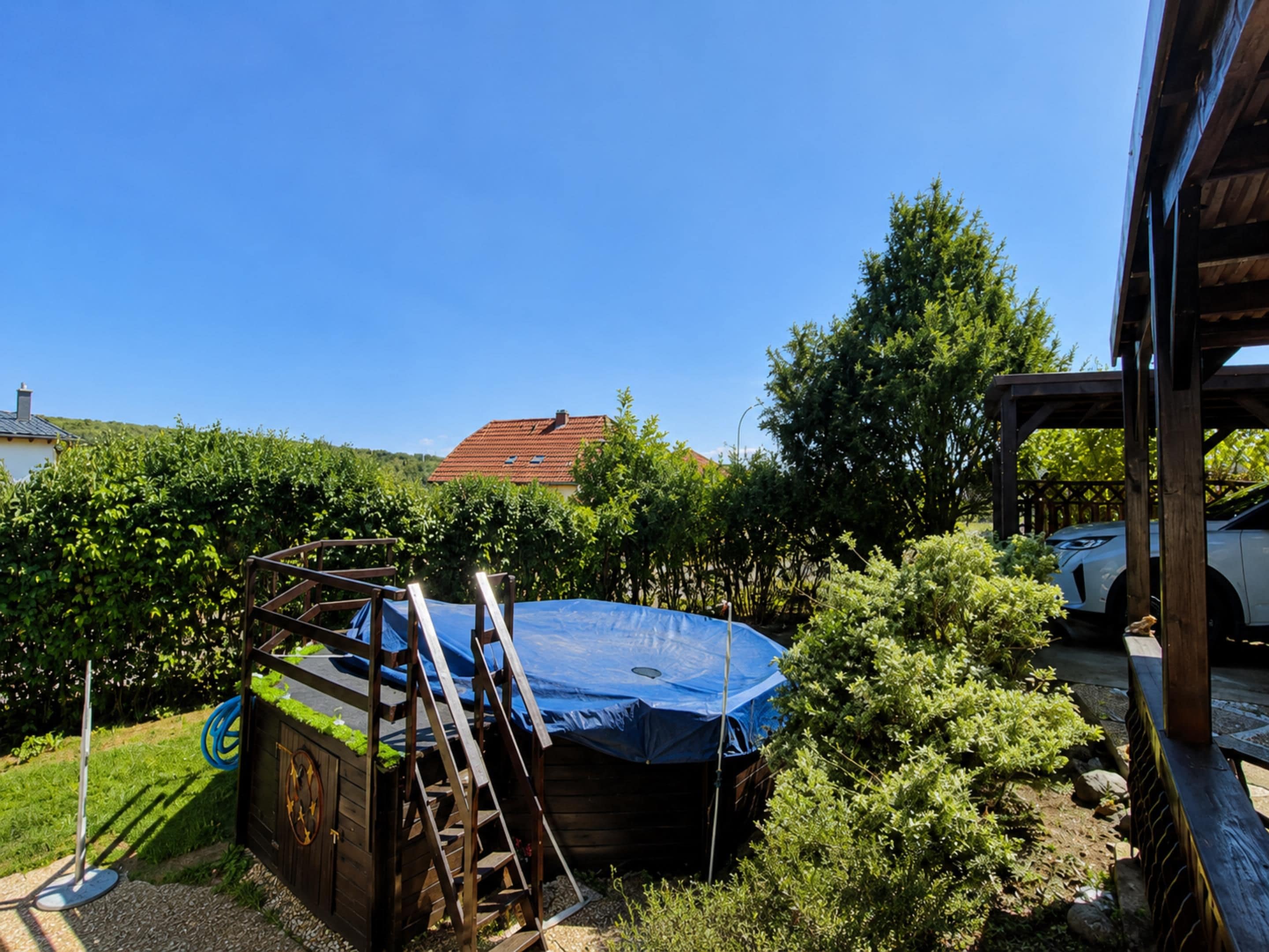 Un jardin avec un trampoline, une terrasse en bois et une voiture garée à proximité.