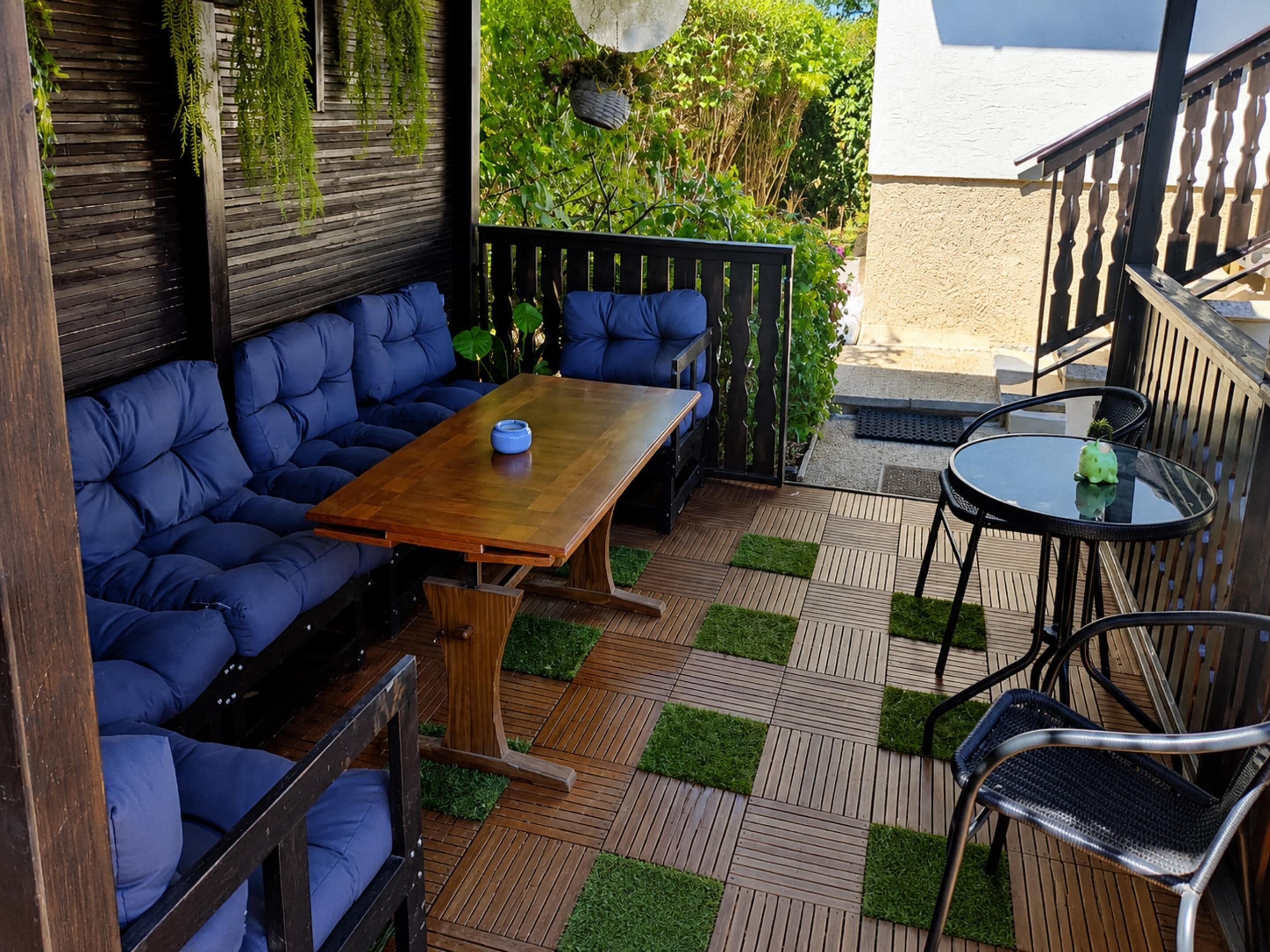 A patio with a wooden table, blue cushioned seating, and a small round table with chairs.