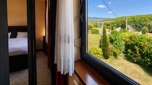 Ein Schlafzimmer mit einem großen Fenster, einem Bett und Blick auf eine grüne Landschaft.
