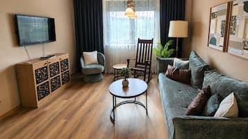 A living room with a sofa, armchair, table, TV, and decorative items.