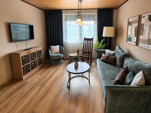 Una sala de estar con sofá, sillón, mesa, televisor y objetos decorativos.