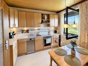 A modern kitchen with wooden cabinets, a built-in oven, and a dining area with a table and chairs.