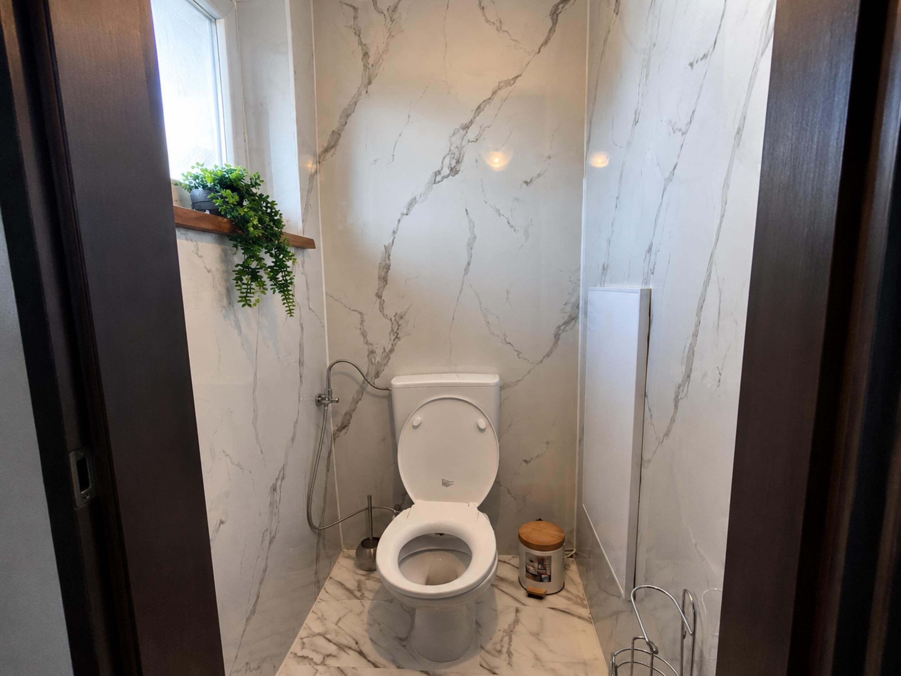 A bathroom with a toilet, a marble floor, and a wall-mounted plant.