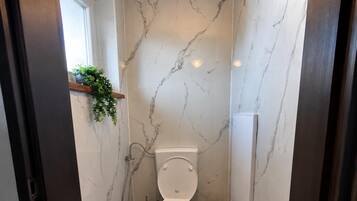 A bathroom with a toilet, a marble floor, and a wall-mounted plant.