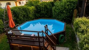 A hexagonal swimming pool with a wooden deck and lounge chairs, surrounded by greenery and residential buildings.