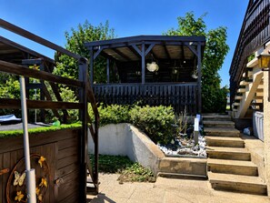 A covered outdoor area with a wooden structure, steps leading up to a building, and a garden with plants and a small water feature. - Private Pool Villa near Oberwart (Miedlingsdorf)