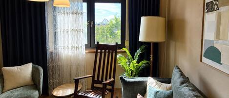 A cozy living room with a rocking chair, a sofa, a side table, and a potted plant.