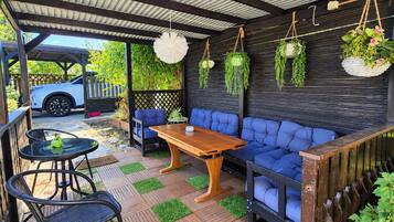 A covered outdoor seating area with a wooden table and blue cushioned seating.