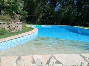 Ein klarer, blauer Pool mit Steinbord und einer Steinmauer im Hintergrund.