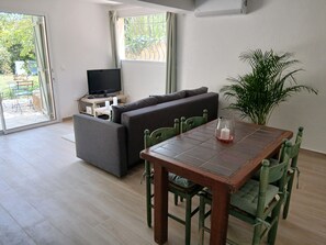 A living room with a sofa, a television on a stand, a dining table with chairs, and a potted plant. - Rose Stone: 2-Bedroom Apartment with Pool, Where Land Meets Sea on the Riviera (Opio)