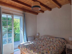 Une chambre avec un plafond en bois, un lit recouvert d’une couvre-lit à motifs floraux, une table de chevet avec une lampe et une fenêtre avec des rideaux.