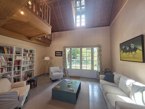 Ein geräumiges Wohnzimmer mit hoher Decke, einem großen Bücherregal, einem bequemen Sofa, einem Couchtisch und einem Gemälde an der Wand.