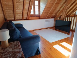 Une pièce chaleureuse avec un plafond en bois, un canapé, une télévision et une lampe.