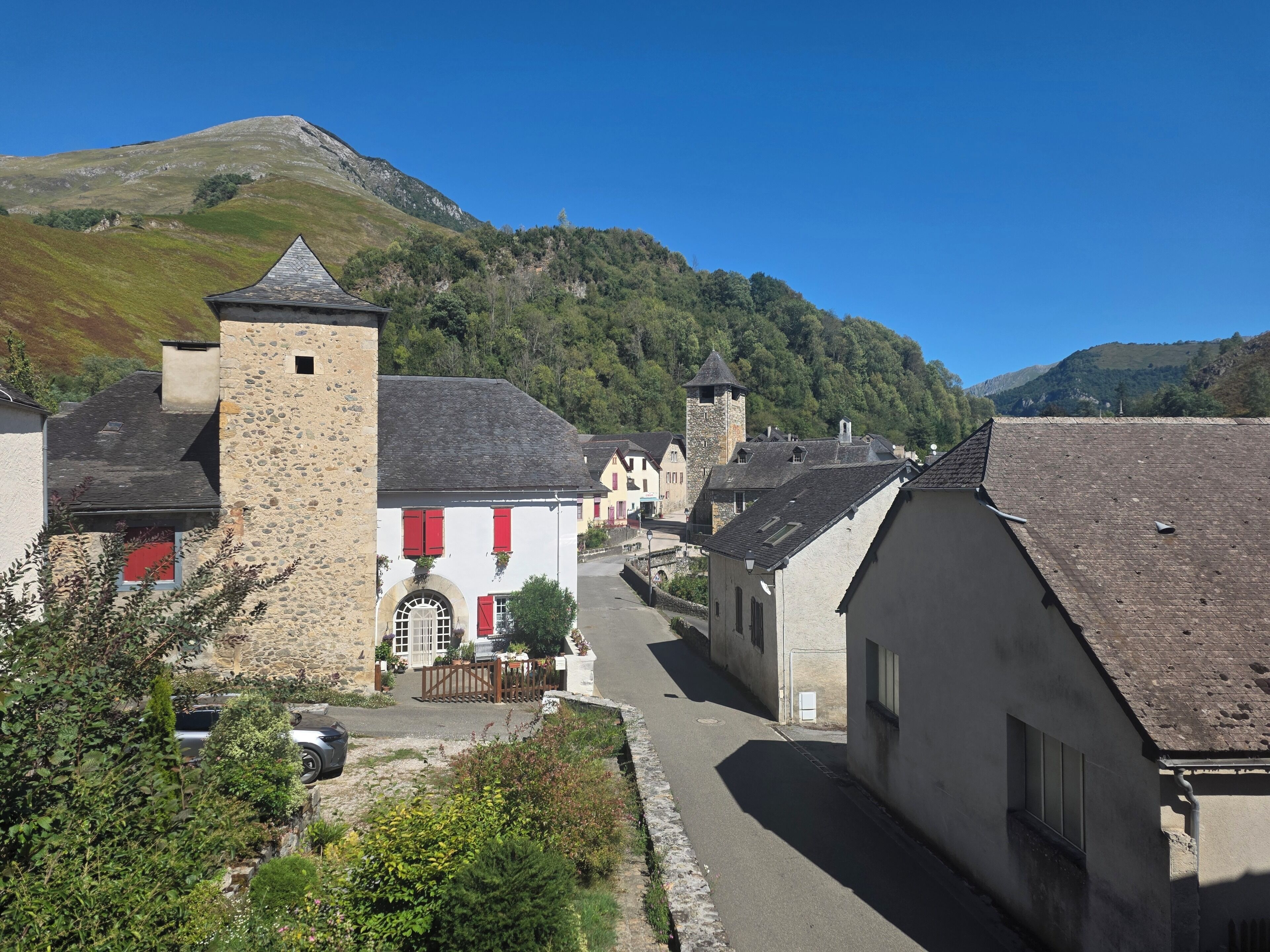 Eine enge Straße mit traditionellen Steinhäusern, einem markanten Turm und einer gebirgigen Kulisse.