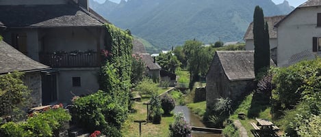 A traditional village with stone buildings, a clear stream, and mountains in the background.