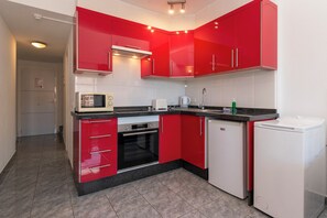 A compact kitchen with red cabinets, a microwave, a toaster, a sink, and a refrigerator. - Central 1 Bedroom Apartment. Communal Heated Pool (Los Cristianos)