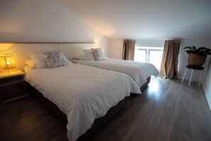 Ein Hotelzimmer mit zwei Betten, einem Nachttisch mit Lampe, einem Fenster mit Vorhängen und einer Topfpflanze auf einem kleinen Tisch.