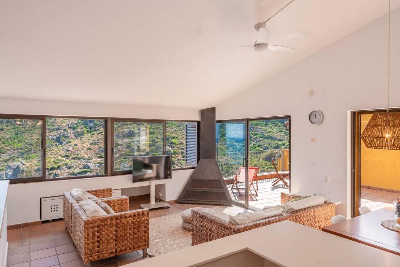 Een moderne woonkamer met een open haard, grote ramen, rieten meubels en een flatscreen televisie.