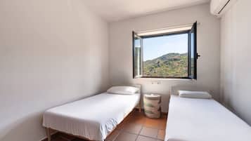 Quarto pequeno e limpo com duas camas de solteiro, uma janela com vista para uma paisagem montanhosa e um ar condicionado.