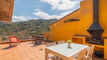 Um terraço com mesa, cadeiras, churrasqueira e vista para uma paisagem montanhosa.