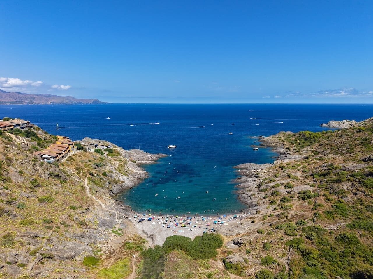 A coastal landscape with a rocky beach, clear blue sea, and a few boats.