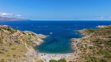 A coastal landscape with a rocky beach, clear blue sea, and a few boats.