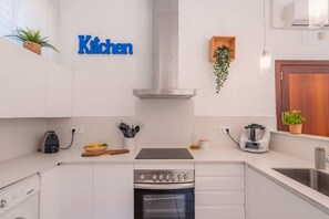 A modern kitchen with white cabinetry, a stainless steel range hood, a built-in oven, and a coffee maker.