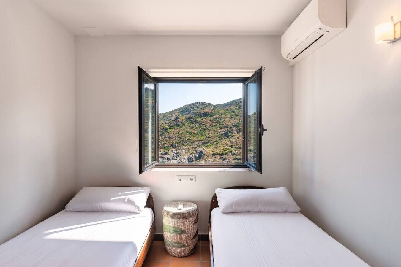 Une petite pièce avec deux lits, une fenêtre donnant sur un paysage montagneux et un climatiseur fixé au mur.