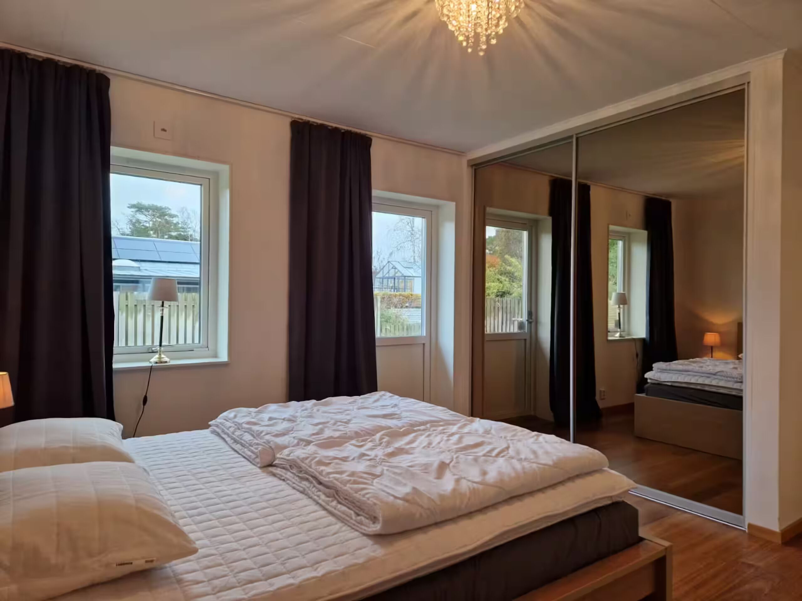 Ein Schlafzimmer mit einem Bett, einer Nachttischlampe, einem Fenster und einer Schiebetür, die auf einen Balkon führt.