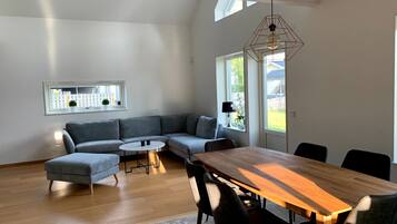 Ein zeitgemäßer Wohnbereich mit einem Ecksofa, einem runden Couchtisch, einem Esstisch mit Stühlen und einer Pendelleuchte.
