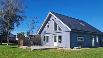 Ein modernes, zweistöckiges Haus mit einem geneigten Dach, einer überdachten Terrasse und einem gepflegten Rasen.