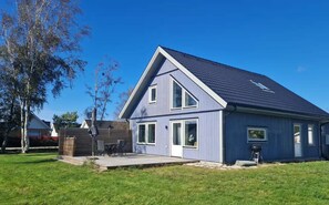 Ein modernes, zweistöckiges Haus mit einem geneigten Dach, einer überdachten Terrasse und einem gepflegten Rasen.