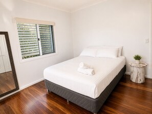 A bedroom with a bed, a window with blinds, a round side table with a plant, and a mirror on the wall. - Charming Queenslander 3 bed 1 bath in West End (West End)