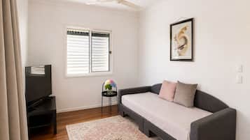 A living room with a sofa, a television, a ceiling fan, a window with blinds, and a framed artwork on the wall.